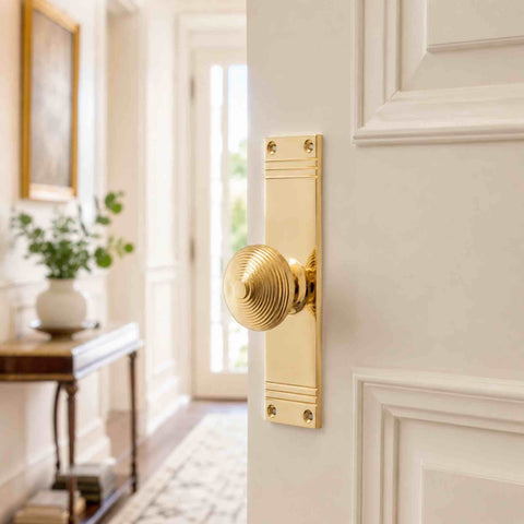 Polished brass beehive door knob with tall reeded backplate fitted to a traditional white panelled internal door.
