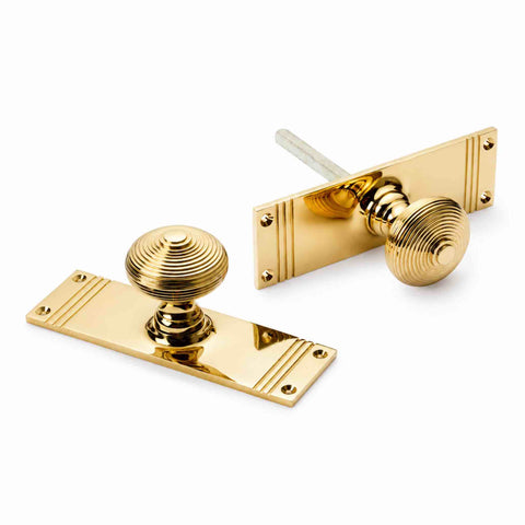 Polished brass reeded beehive mortice door knob pair with tall rectangular backplates, spindle and fixing holes.