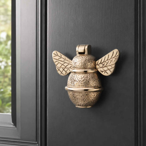 Polished brass bumble bee door knocker mounted on a black panelled entrance door