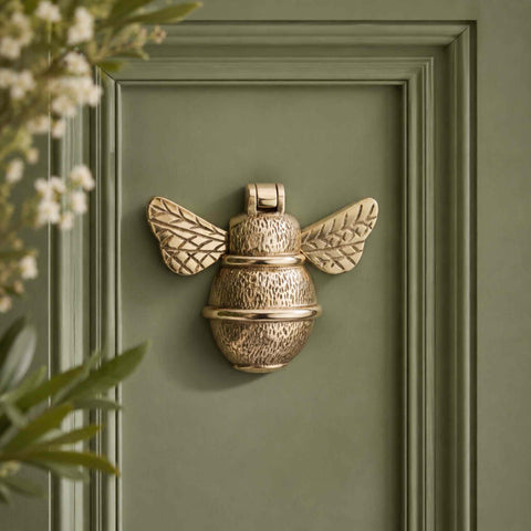 Polished brass bumble bee door knocker fitted to a sage green front door with decorative panelling