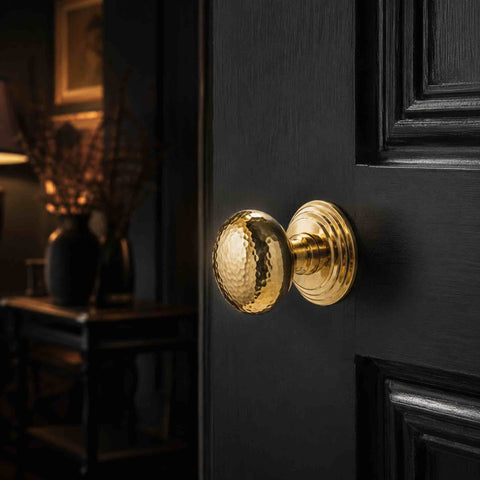 Polished brass hammered mortice door knob with stepped backplate fitted to a black panelled interior door