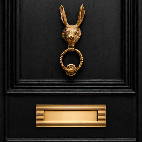 Polished brass hare door knocker with reeded ring fitted to a black panelled front door above a brass reeded letter plate.