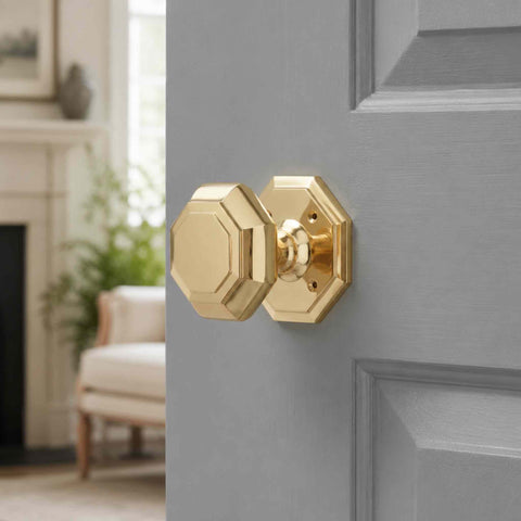 Polished brass octagonal door knob fitted to a grey internal door in a bright home interior