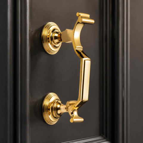 Polished brass reeded doctor door knocker mounted on a black front door, showcasing the polished brass finish and decorative reeded backplates.