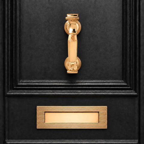 Front-facing polished brass reeded doctor door knocker installed above a matching reeded letter plate on a black entrance door.