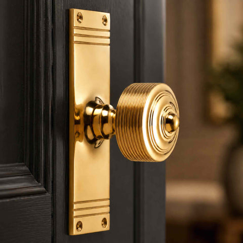 Polished brass reeded door knob on backplate fitted to a black panelled door, showcasing the decorative reeded detailing and bright brass finish.