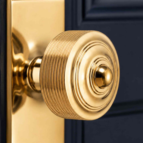 Close-up of a polished brass reeded door knob on matching backplate, highlighting the precision-machined reeded design and reflective finish.