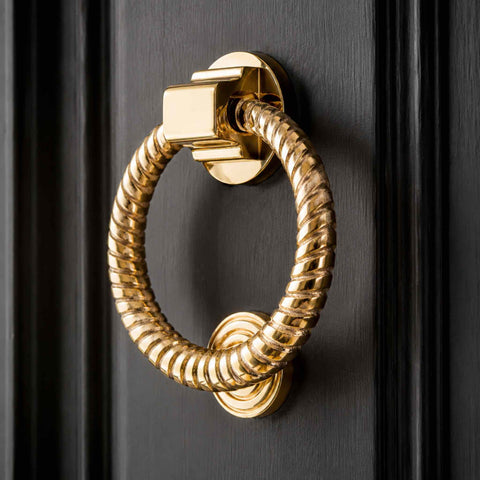 Close-up of polished brass reeded ring door knocker mounted on a dark entrance door