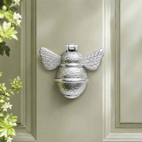 Polished Chrome Bumble Bee Door Knocker fitted to a sage green front door with decorative garden foliage in the foreground