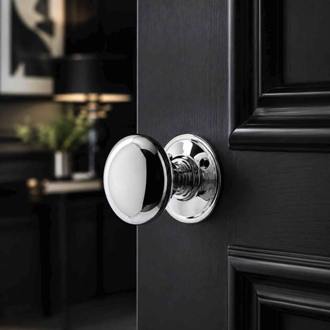 Polished chrome cottage door knob on a round backplate fitted to a black panelled internal door.