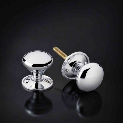 Polished chrome cottage rim and mortice door knob pair with round backplates and threaded spindle on a dark background.