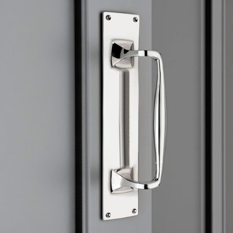 Polished chrome door pull handle mounted vertically on a door, fixed to a rectangular backplate.