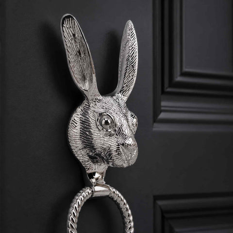 Close-up side view of a polished chrome hare door knocker mounted on a black entrance door, highlighting the intricate fur detailing and reeded ring.