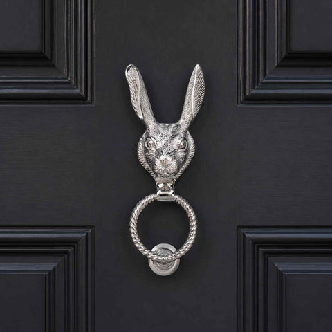 Front-facing polished chrome hare door knocker installed on a black panelled door, featuring a decorative reeded ring and matching strike plate.