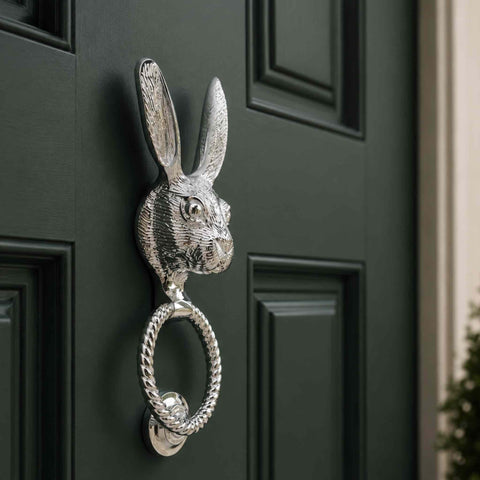 Angled lifestyle shot of a polished chrome hare door knocker on a dark green front door, demonstrating its premium finish and elegant appearance.