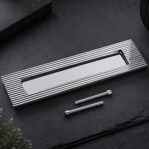 Polished chrome reeded solid brass letter box plate with fixing bolts on a dark stone surface
