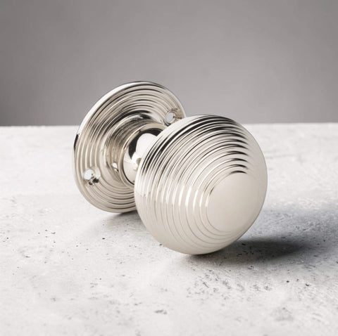 Single polished nickel reeded beehive mortice door knob resting on textured surface with decorative reeded rose