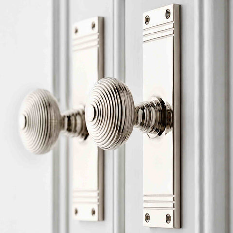 Close-up of polished nickel reeded beehive door knob pair on tall rectangular backplates fitted to white internal doors.