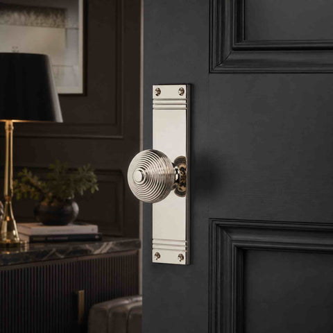 Polished nickel beehive mortice door knob on a tall reeded backplate fitted to a dark panelled internal door.