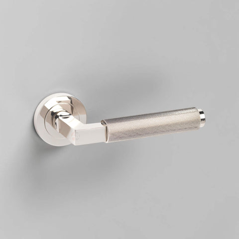 Sprung polished nickel knurled lever door handle mounted on a grey internal door.