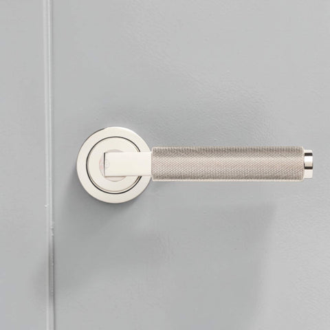 Side profile of polished nickel knurled lever door handle with round rose backplate.