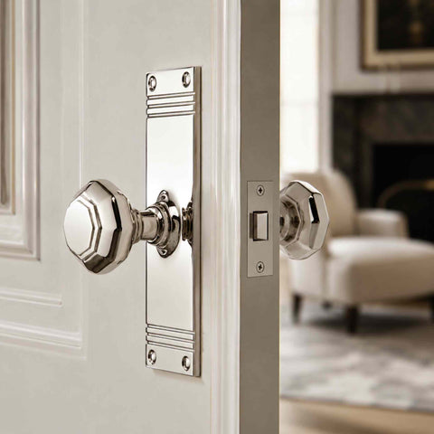 Polished nickel octagonal door knob pair on tall backplates fitted to a white internal door with latch visible