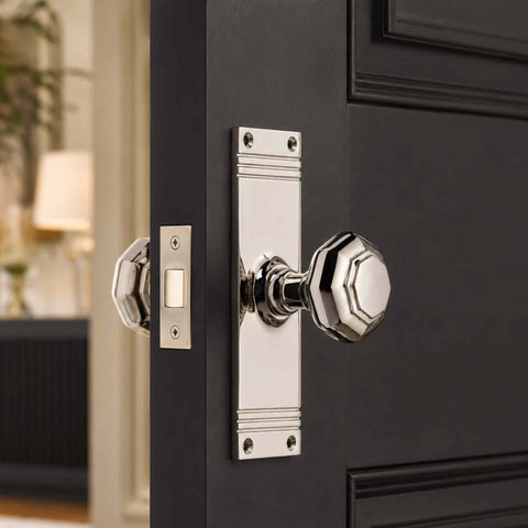 Polished nickel octagonal door knob on a tall reeded backplate fitted to a dark painted internal door with mortice latch.