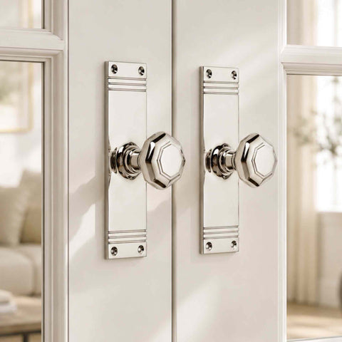 Pair of polished nickel octagonal door knobs on tall reeded backplates fitted to white glazed internal double doors.