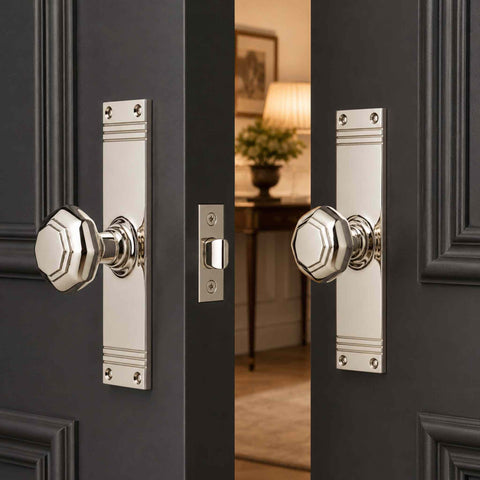 Polished nickel octagonal door knob pair on tall reeded backplates fitted to dark panelled double doors with mortice latch.