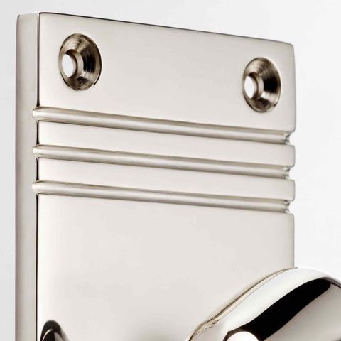Close-up of polished nickel door knob backplate showing reeded detailing and countersunk fixing holes.
