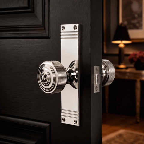 Polished nickel reeded door knob pair on tall backplate fitted to a black panelled door, showcasing the bright polished nickel finish and traditional reeded detailing.