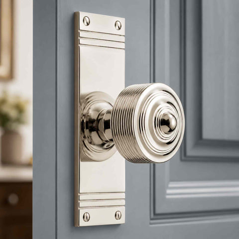 Polished nickel reeded door knob on tall backplate installed on a light grey panelled door, highlighting the elegant finish and period-inspired design.