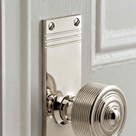 Detailed close-up of a polished nickel reeded door knob and tall backplate, showcasing the smooth polished finish and traditional reeded pattern.
