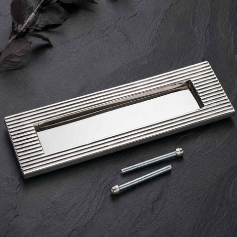 Polished nickel reeded letter box plate displayed with supplied fixing bolts on a dark stone surface