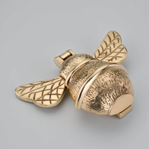 Unlacquered polished brass bumble bee door knocker shown at an angle, highlighting textured body, smooth bands and engraved wing detail.