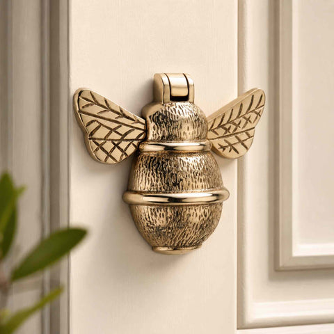 Unlacquered polished brass bumble bee door knocker mounted on a cream painted entrance door
