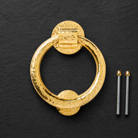 Solid brass hammered ring door knocker with fixing bolts displayed on a black background.