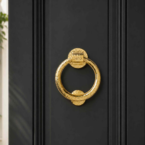 Front view of polished brass hammered ring door knocker fitted to a black panelled entrance door.