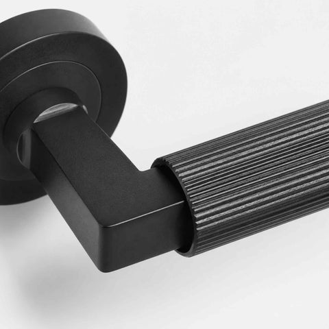 Detailed macro view of black reeded lever handle showing the precision-machined square neck and textured grip design.