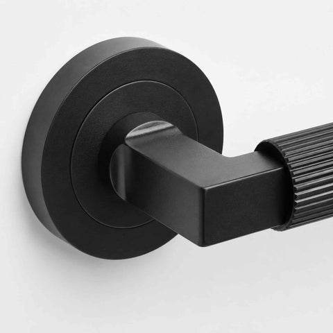 Detailed macro view of black reeded lever door handle highlighting the square neck design and precision-machined grip.