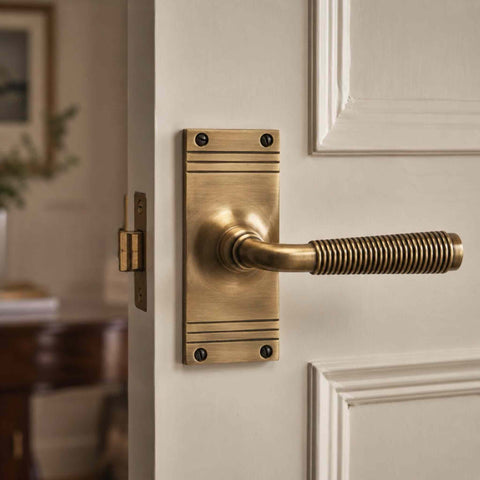 Antique brass reeded lever handle mounted on a white panelled door, demonstrating the contrast between the warm brass tones and light décor.