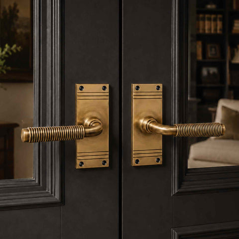 Pair of antique brass reeded lever door handles on black glazed double doors, highlighting the warm antique brass finish against dark woodwork.