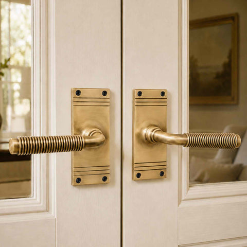 Pair of antique brass reeded lever door handles fitted to white glazed double doors, creating a classic and timeless interior look.