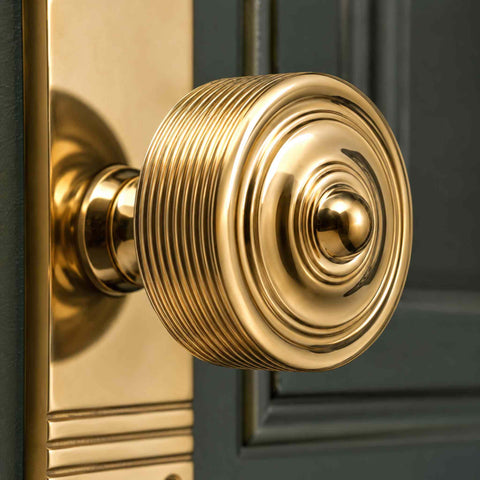 Reeded polished brass door knob pair on tall backplate fitted to a black panelled door, showcasing the traditional reeded design and bright polished brass finish.