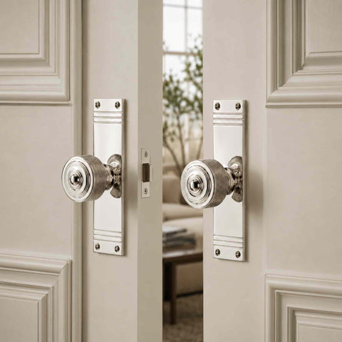 Reeded polished nickel door knob pair on tall backplates installed on white internal double doors, demonstrating the classic design in a bright interior setting.