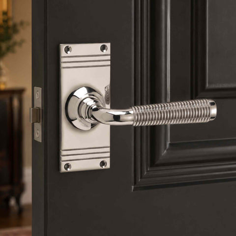 Polished nickel reeded lever door handle on backplate fitted to a black panelled door, showcasing the bright polished finish and detailed reeded grip.
