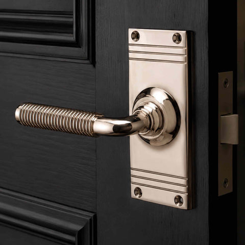 Close-up of the polished nickel reeded lever handle showing the decorative reeded grip and smooth curved lever design on a dark coloured door.