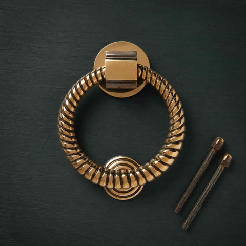 Aged brass reeded ring door knocker with matching fixing bolts on dark background
