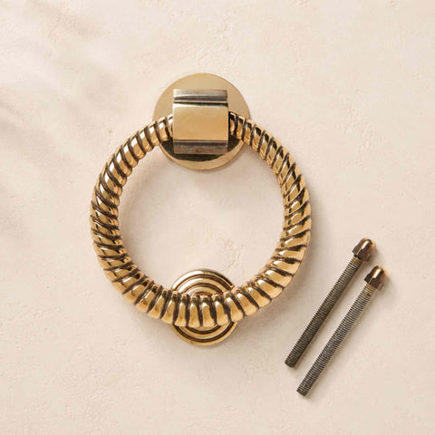 Aged brass reeded ring door knocker with fixing bolts on light textured background