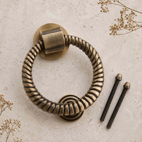 Antique Brass Reeded Ring Door Knocker with matching fixing bolts on a stone background